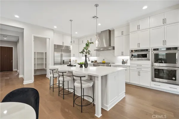 a kitchen with stainless steel appliances kitchen island granite countertop a stove a sink a refrigerator and white cabinets with wooden floor