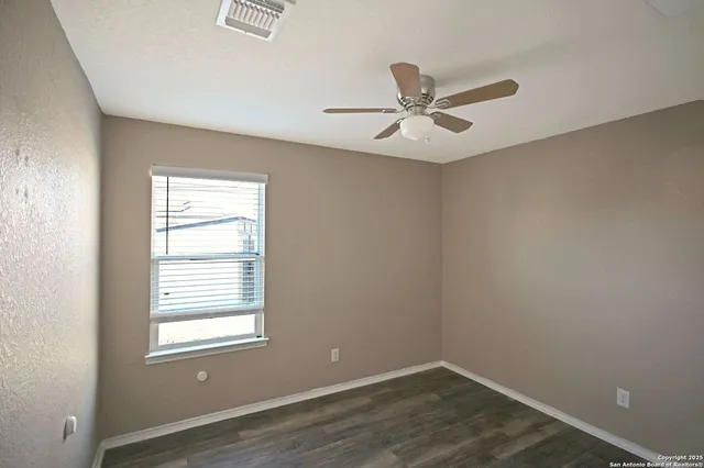 an empty room with wooden floor ceiling fan and windows