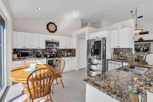 a kitchen with stainless steel appliances granite countertop a stove top oven a refrigerator a sink a dining table and chairs with wooden floor