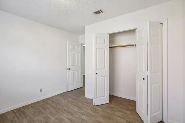 a view of an empty room with wooden floor and closet area