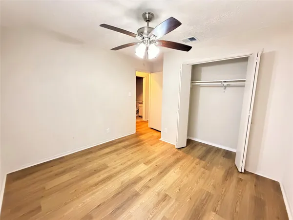 a view of an empty room with wooden floor and a ceiling fan