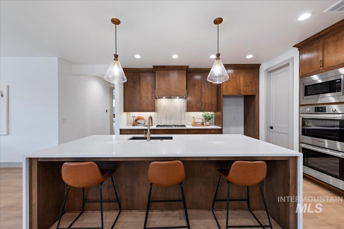 967 West Malbar Street Meridian, ID 83646 - Photo 10 of 33 Kitchen featuring light wood finished floors, light stone counters, stainless steel appliances, and decorative backsplash