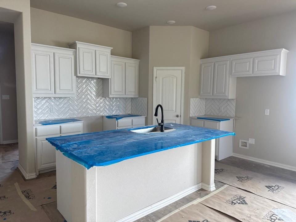1228 Colca Drive Springtown, TX 76082 - Photo 3 of 9 Kitchen island with an undermount sink and a matte black faucet, surrounded by white cabinetry, a herringbone pattern tile backsplash, and recessed ceiling lighting