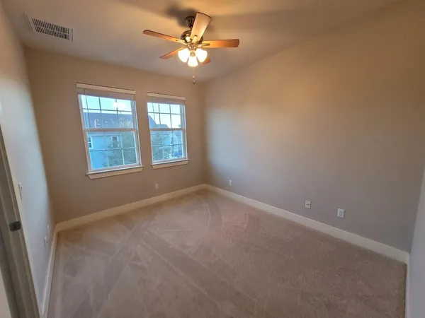 an empty room with a chandelier fan and windows