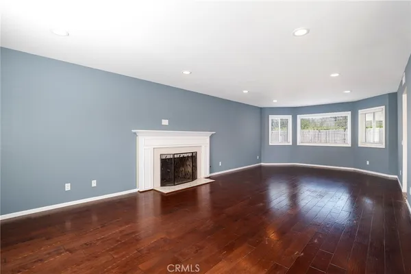 an empty room with wooden floor fireplace and windows