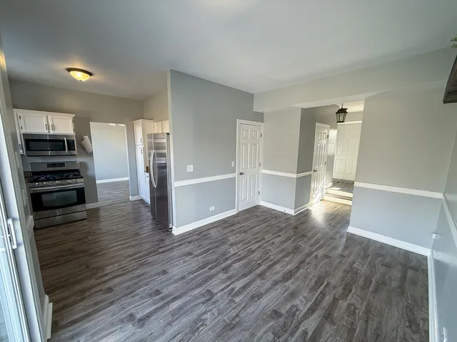 an empty room with wooden floor and a kitchen