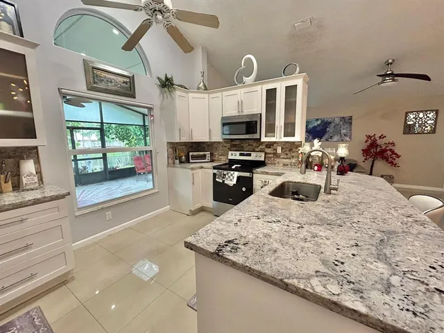 a kitchen with stainless steel appliances kitchen island granite countertop a stove top oven a sink a dining table and chairs with the floor to ceiling window