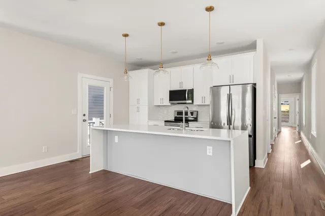 a kitchen with stainless steel appliances granite countertop a refrigerator a stove a microwave oven a sink dishwasher and white cabinets with wooden floor