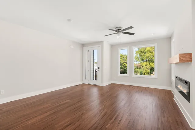 an empty room with wooden floor chandelier fan and windows
