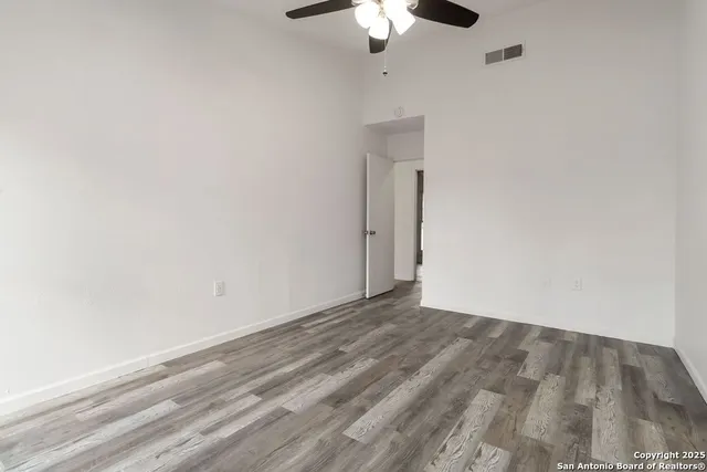 an empty room with a chandelier fan and wooden floor