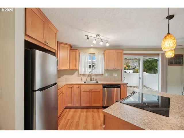 a kitchen with stainless steel appliances granite countertop a refrigerator a sink dishwasher a stove and a dining table with wooden floor