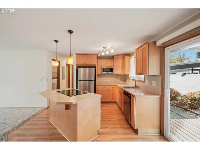 a open kitchen with stainless steel appliances kitchen island granite countertop a refrigerator a stove a sink and white cabinets with wooden floor