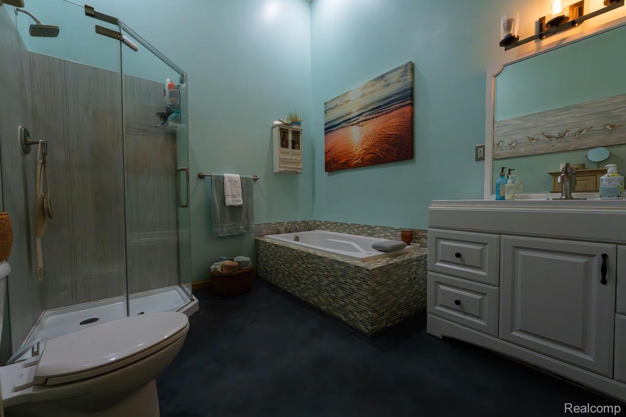 2418 South 41st Road South Cadillac, MI 49601 - Photo 19 of 57 Bathroom featuring a glass-enclosed shower with panel walls, a built-in tub with a mosaic tile surround, a single vanity with a white countertop, and dark-toned flooring