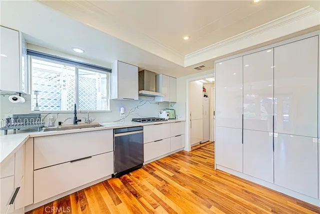 a large kitchen with a refrigerator a sink dishwasher a stove and white cabinets with wooden floor