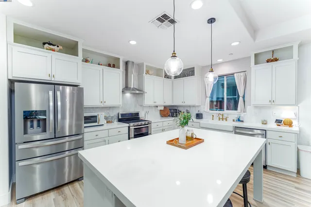 a kitchen with stainless steel appliances a stove a sink a refrigerator white cabinets and wooden floor