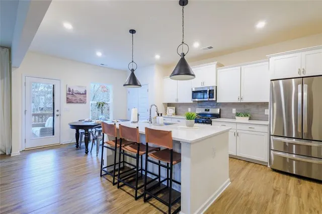 a kitchen with stainless steel appliances granite countertop a refrigerator a stove a sink dishwasher a dining table and chairs with wooden floor