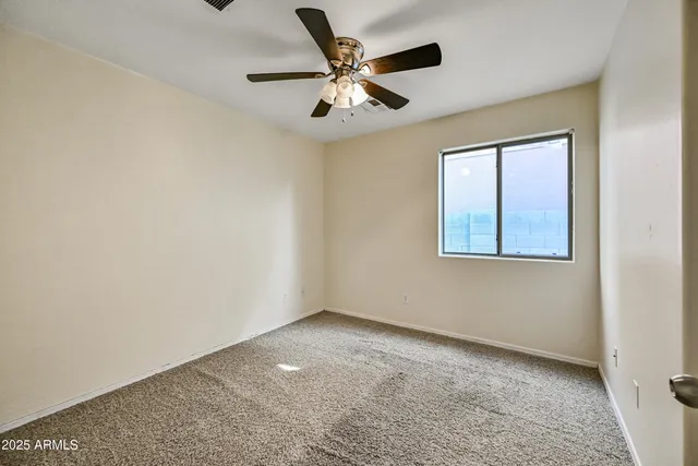 an empty room with ceiling fan and windows