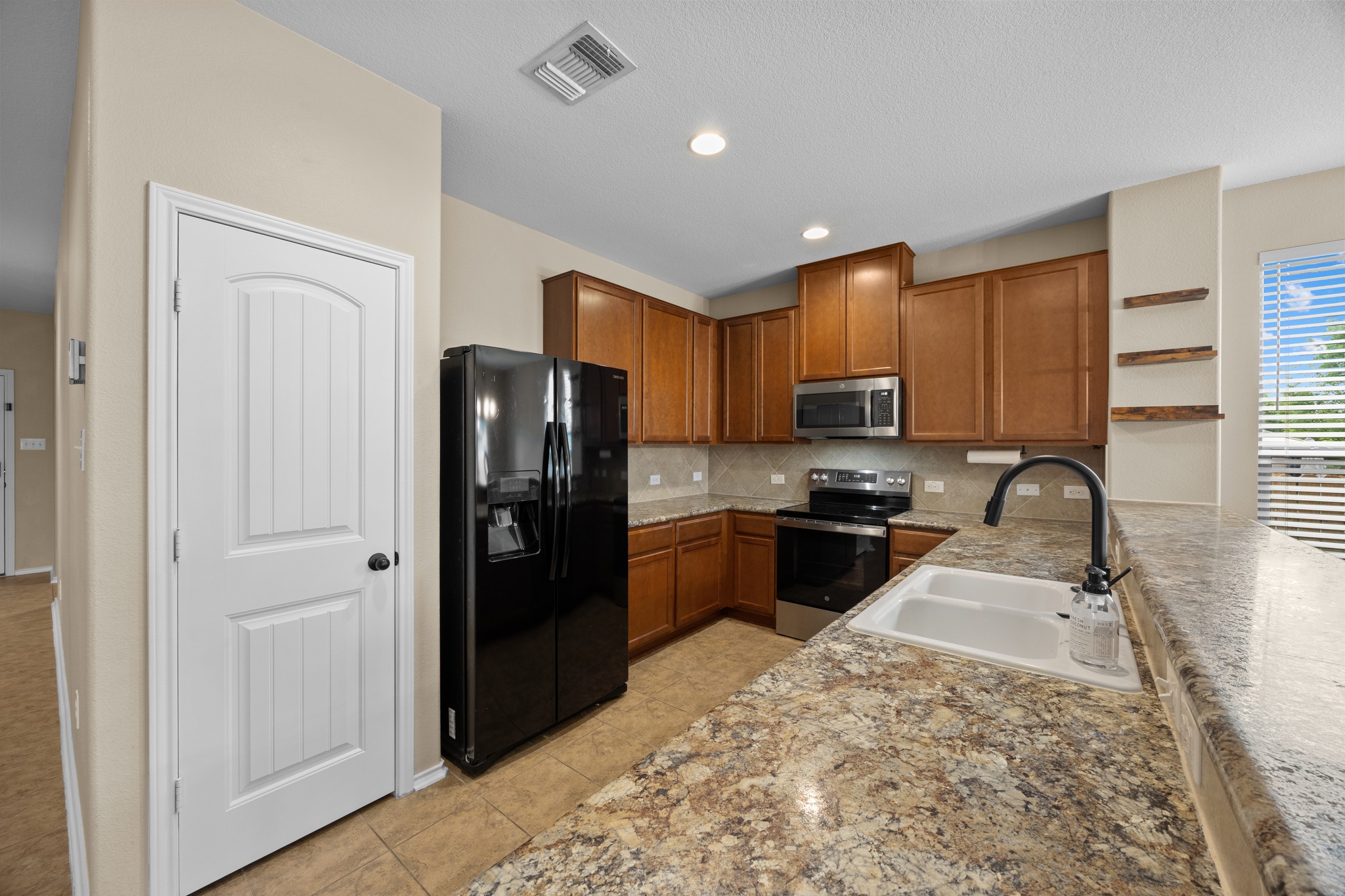 1125 Yellow Iris Road Leander, TX 78641 - Photo 18 of 31 Kitchen featuring stainless steel appliances, wood finish cabinetry, tasteful backsplash, light tile patterned floors, and a peninsula