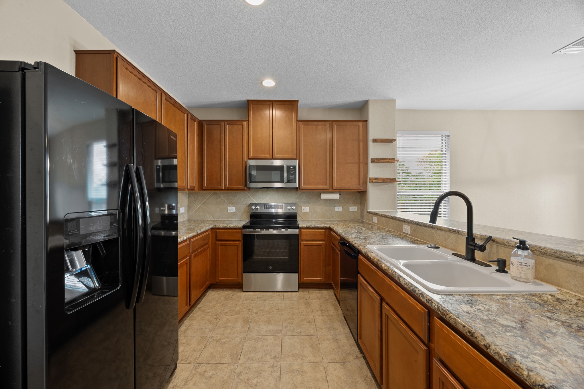 1125 Yellow Iris Road Leander, TX 78641 - Photo 19 of 31 Kitchen featuring black appliances, wood finish cabinets, light stone counters, recessed lighting, and decorative backsplash