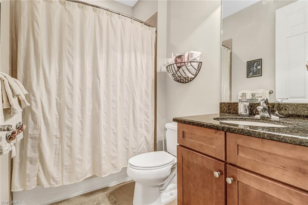 8997 Cambria Circle, Unit 2002 Naples, FL 34113 - Photo 30 of 35 a bathroom with a granite countertop sink a toilet and a shower curtain