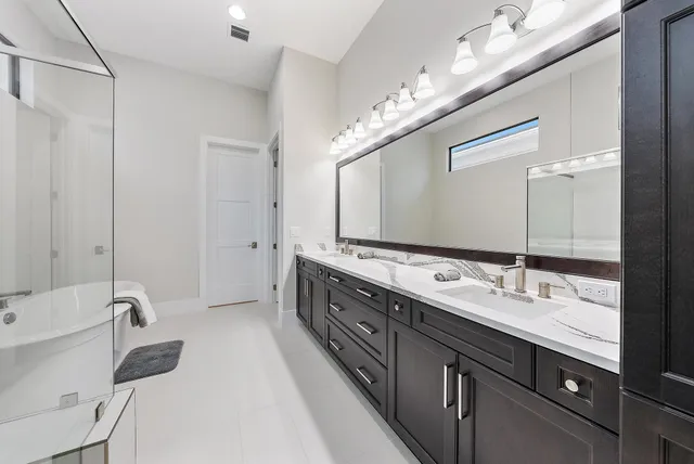 a bathroom with a double vanity sink a large mirror and a bathtub