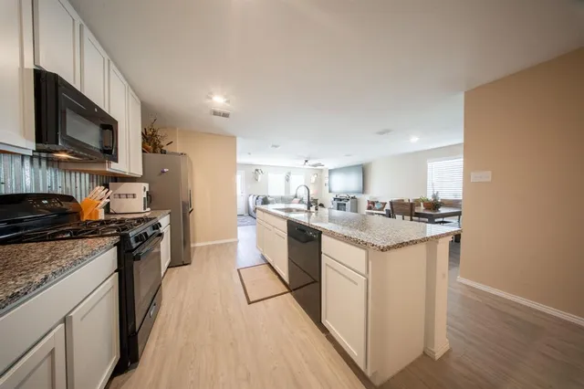 a kitchen with stainless steel appliances granite countertop a stove top oven a sink dishwasher and a refrigerator with wooden floor