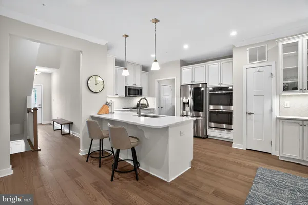 a kitchen with stainless steel appliances a stove top oven a refrigerator a dining table and chairs with wooden floor