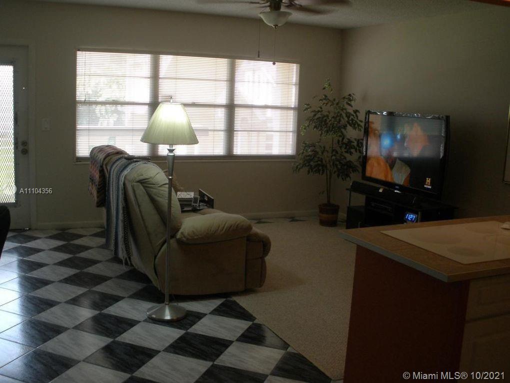 195 Fanshaw East, Unit 195 Boca Raton, FL 33434 - Photo 2 of 12 a living room with furniture a flat screen tv and a floor to ceiling window