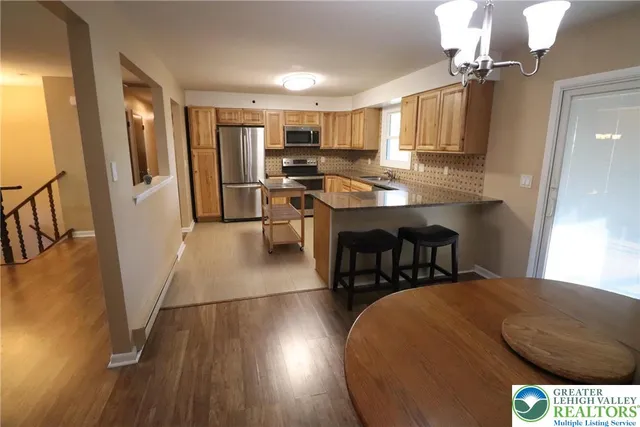 a kitchen with stainless steel appliances granite countertop a stove a refrigerator a sink a dining table and chairs with wooden floor