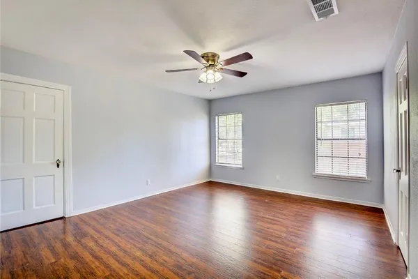 an empty room with wooden floor chandelier fan and windows