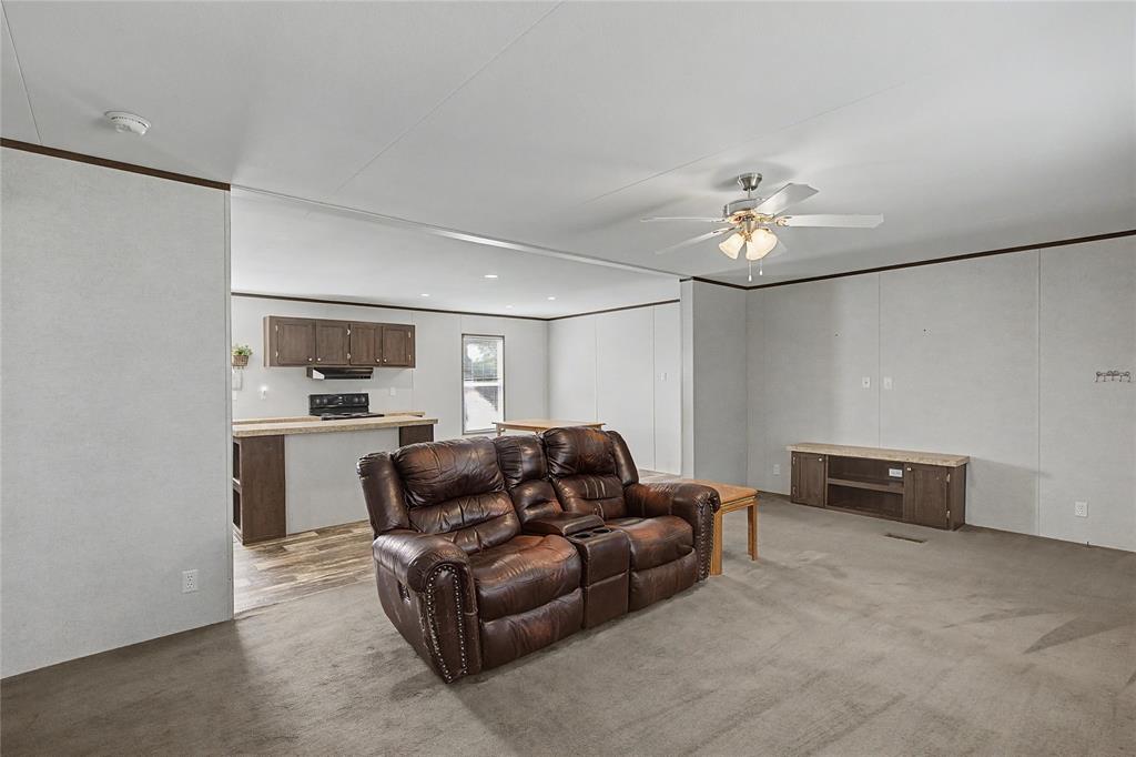 177 New Highland Road Springtown, TX 76082 - Photo 11 of 40 Open concept living space featuring neutral wall tones, dark trim accents, a ceiling fan with integrated lighting, and carpet flooring