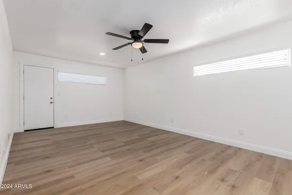 a view of an empty room with wooden floor and a ceiling fan