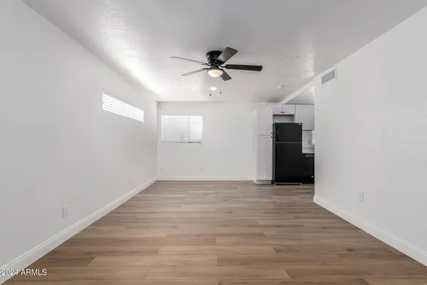 an empty room with wooden floor ceiling fan and windows