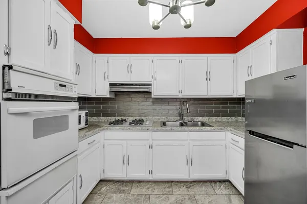 a kitchen with stainless steel appliances granite countertop a refrigerator a sink dishwasher a stove with white cabinets and wooden floor