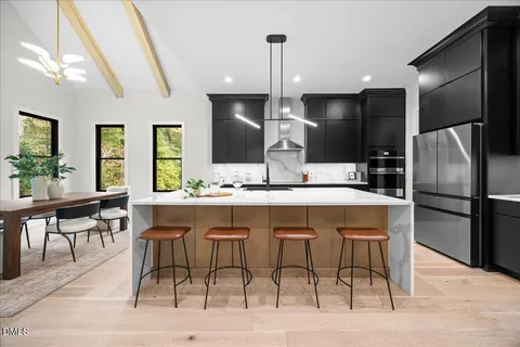 a kitchen with stainless steel appliances kitchen island granite countertop a dining table chairs and a refrigerator