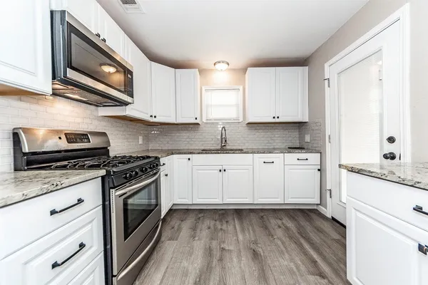 a kitchen with stainless steel appliances granite countertop a stove a sink and white cabinets