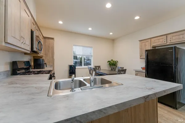 a kitchen with stainless steel appliances kitchen island granite countertop a refrigerator a stove and a sink with wooden floor