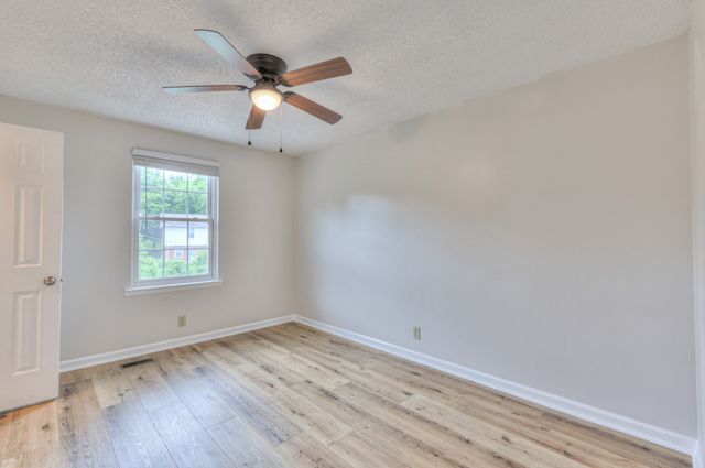 an empty room with wooden floor ceiling fan and window