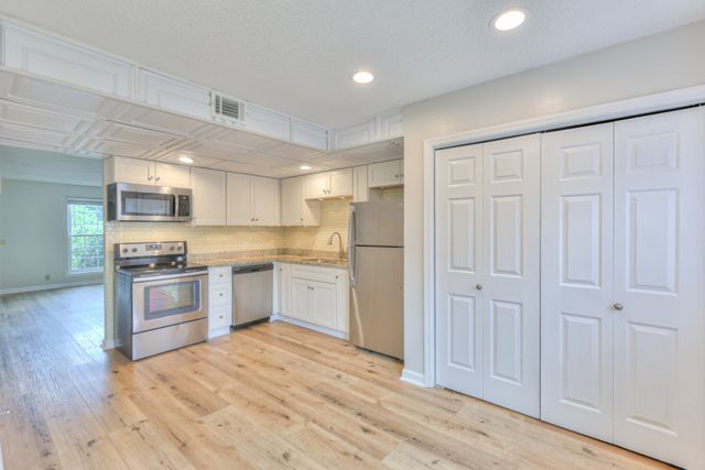 a kitchen with stainless steel appliances granite countertop a refrigerator oven a sink dishwasher and white cabinets with wooden floor