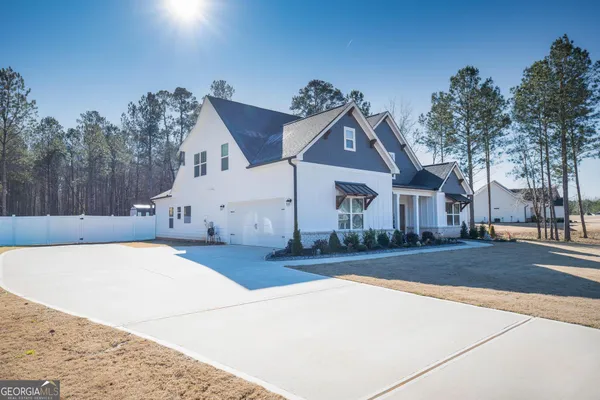 a view of a white house next to a yard with road and trees