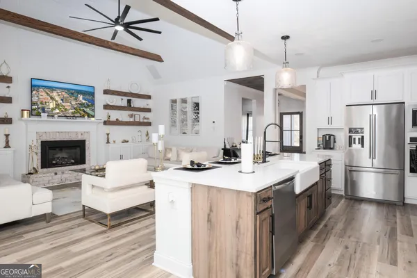 a large white kitchen with a stove a sink dishwasher a refrigerator and a fireplace with wooden floor