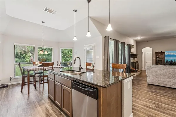 a kitchen with stainless steel appliances granite countertop wooden floor sink stove dining table and chairs