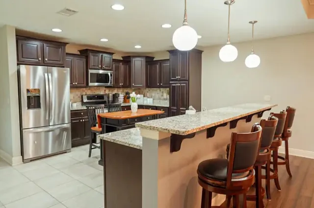 a kitchen with stainless steel appliances granite countertop a sink a stove a refrigerator cabinets and chairs