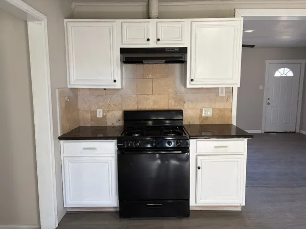 a kitchen with granite countertop white cabinets and black stove