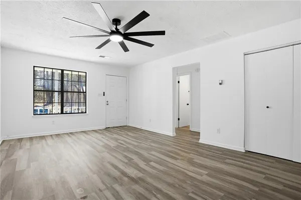 an empty room with wooden floor a ceiling fan and windows