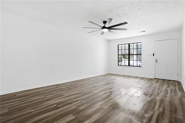 an empty room with wooden floor fan and windows