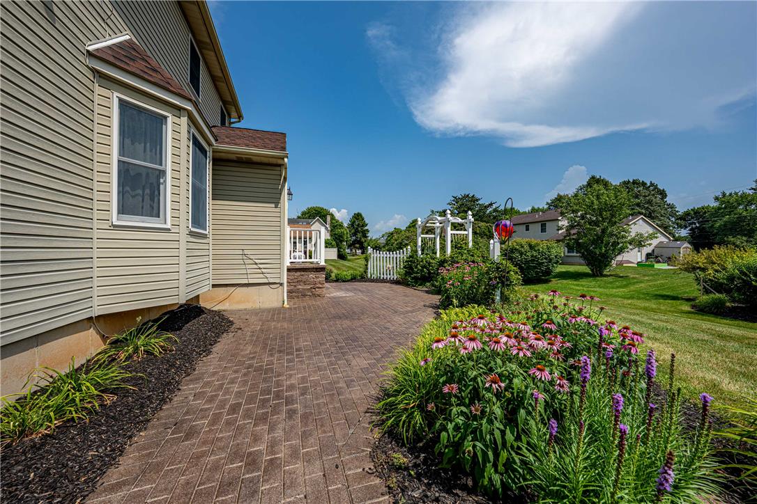 4568 Greenfield Road Bethlehem, PA 18017 - Photo 44 of 59 A neatly manicured lawn with vibrant garden beds leads to a charming brick-paved patio, perfect for outdoor enjoyment.
