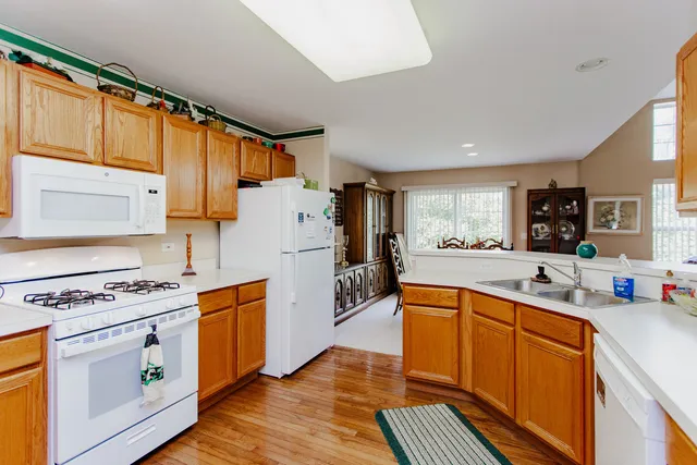 a kitchen with stainless steel appliances granite countertop a refrigerator a sink dishwasher a stove and white countertops with wooden floor