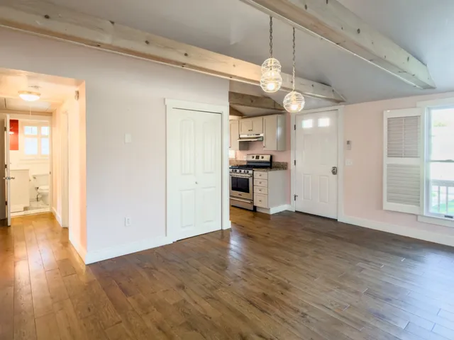 a view of a kitchen and an empty room with wooden floor