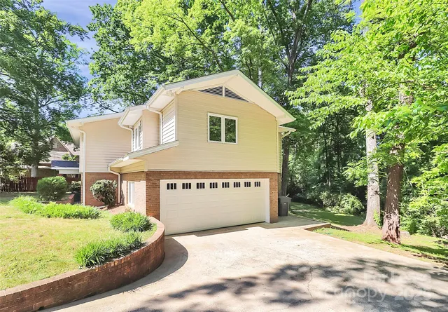 a view of a house with a yard plants and large tree